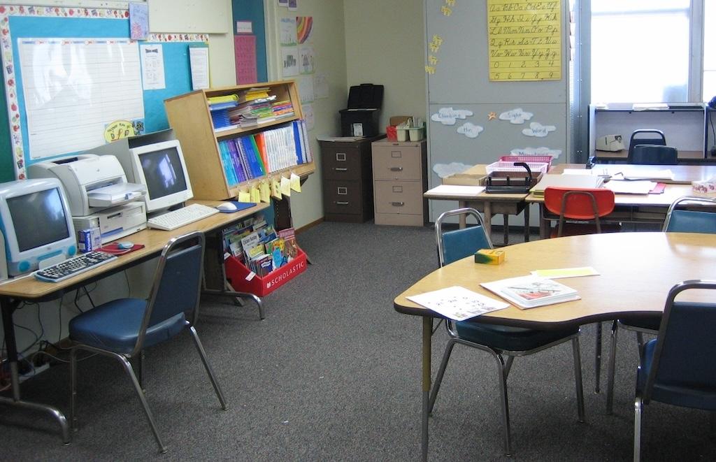Inside an elementary school classroom with computers, desks, chairs, and books