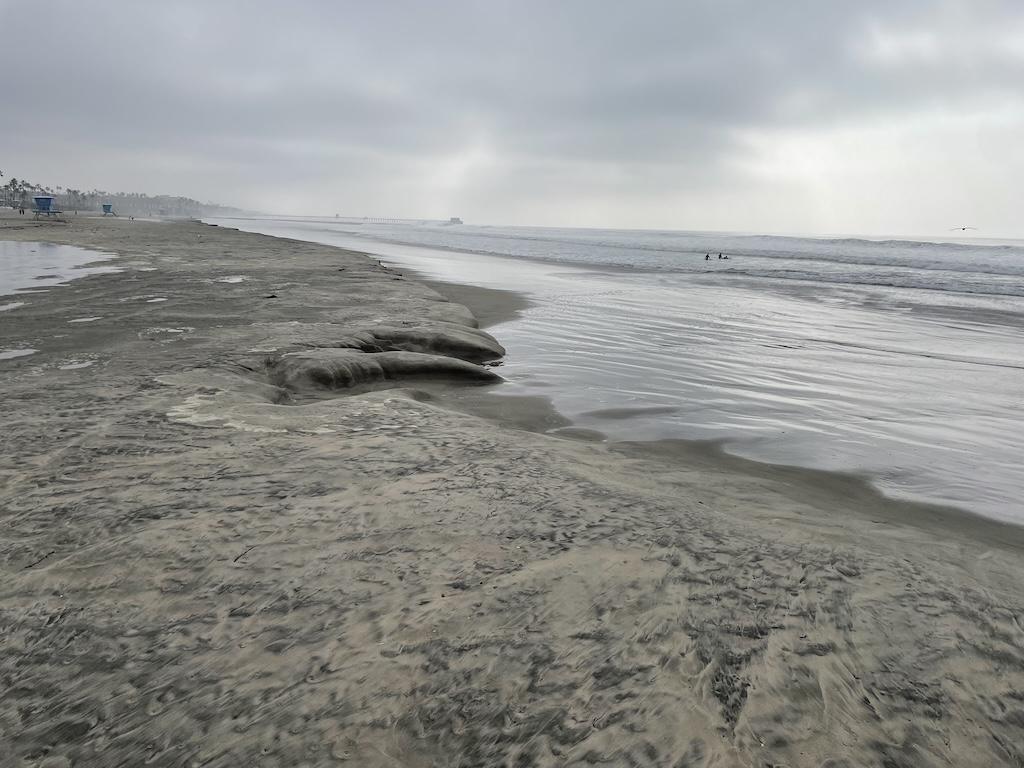 Beautiful ocean view with grey skies and people in the water in the distance at Oceanside Harbor in California
