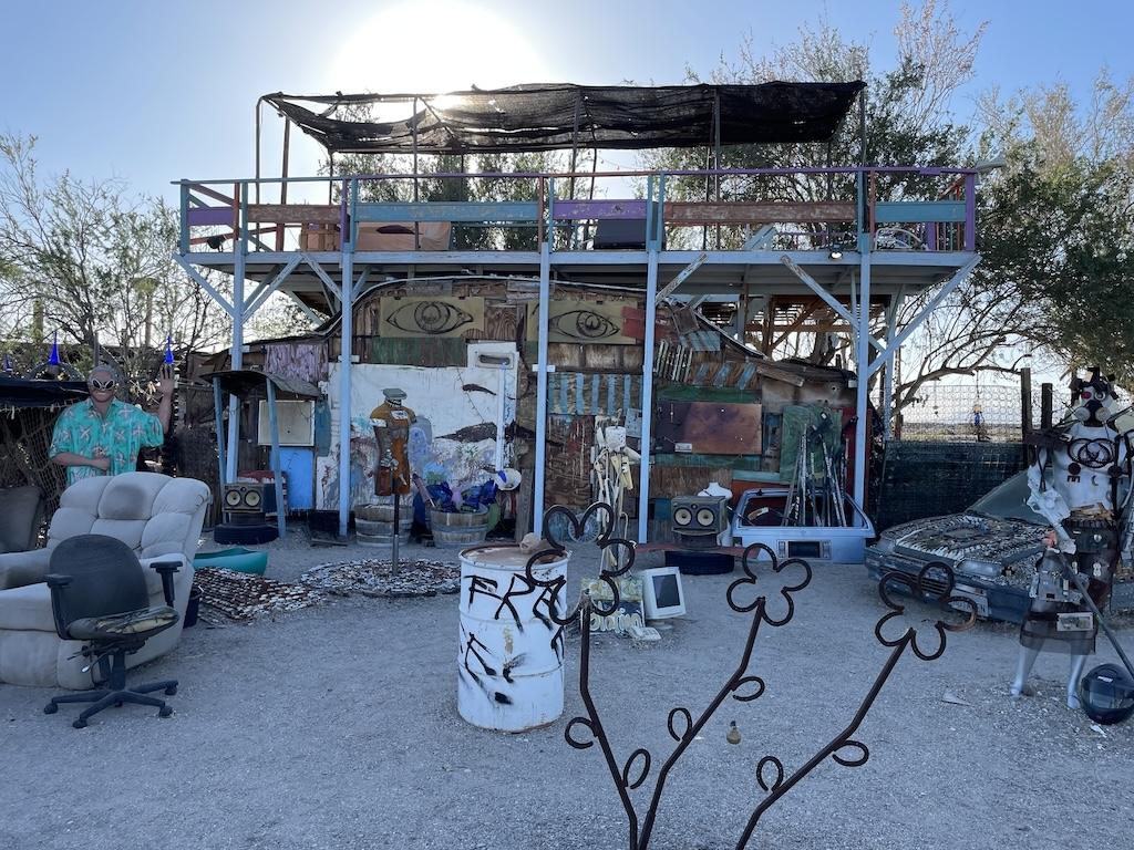 Exhibit of a shelter with random items built at East Jesus, Slab City