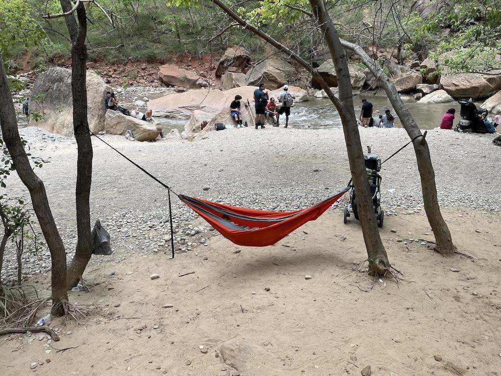 View of hammock tied to tree and people gathered at the river at the Narrows hike in Zion National Park 