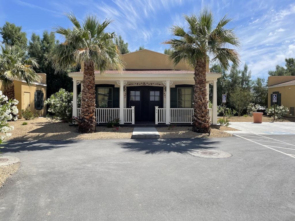 Front view of the cottage where we stayed while visiting Death Valley, with palm trees and flower bushes outside