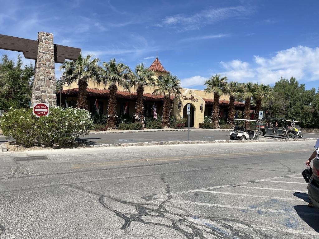 Entrance to the Ranch at Death Valley, Town Hall building with palm trees, flower bushes, and golf carts in front