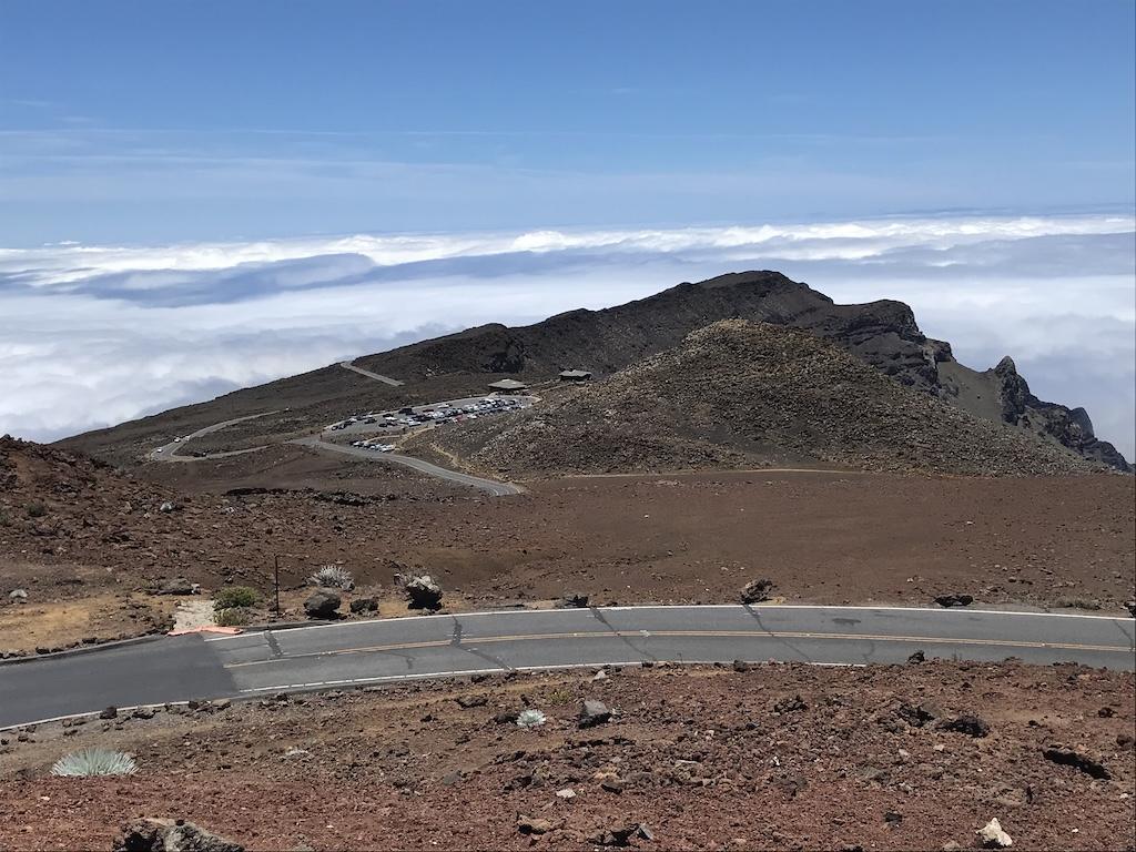 View from Haleakala summit looking downs to see a parking lot in the distance and clouds