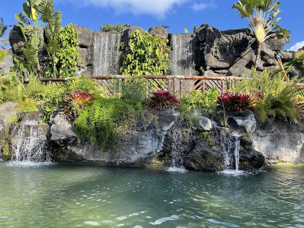 Waterfall with pink flowers and green foilage in the lagoon at the Polynesian Cultural Center, Oahu, Hawaii