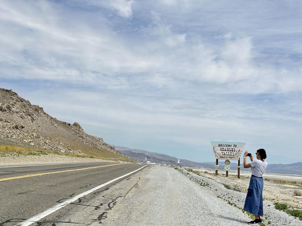 Luna in front of the welcome to Searles Valley sign taking a picture on the side of the road