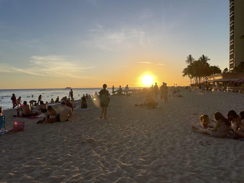 Private beach at The Royal Hawaiian Resort during sunset, with people watching the sunset against a clear sky, on Waikiki Beach, Hawaii