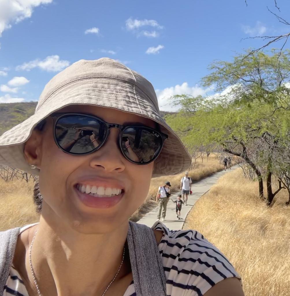 Selfie and close up of Luna smiling to the camera during the Diamond Head Crater hike in Oahu, Hawaii with people walking behind her in the distance