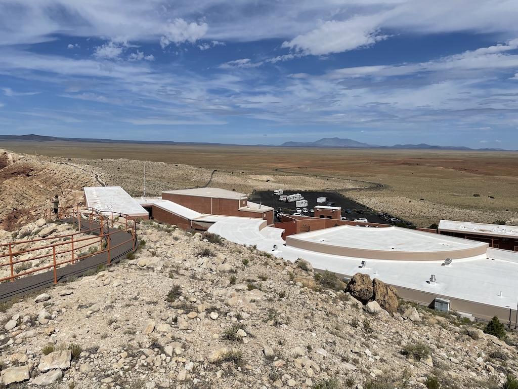 View of Meteor Crater museum and buildings from the top lookout point and a person looking at the crater 
