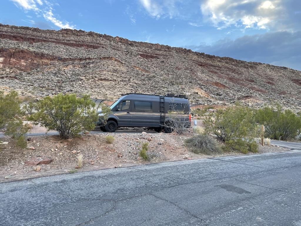 View Luna’s camper van parked at next to red rocks at Quail Creek State Park Campground in Hurricane, Utah.