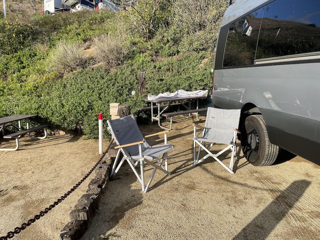 Two camping chairs and picnic table next to Sprinter Van in parking space at Surf Outpost in Malibu, California