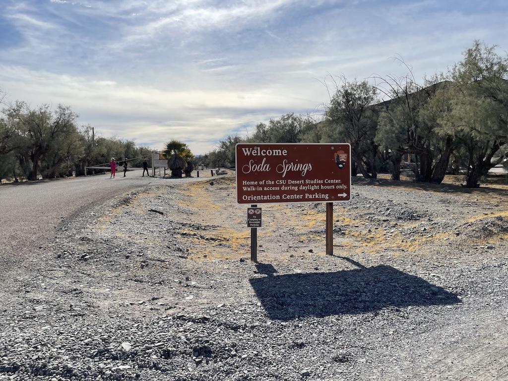 Soda Springs Welcome pointing to parking area, with people walking in the far distance