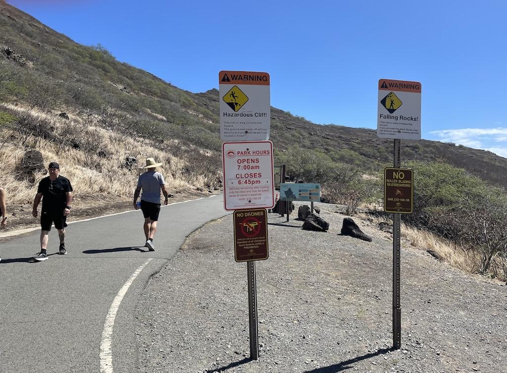 Entrance signs at the Makapu’u Lighthouse hike where people are walking on the trail in Oahu, Hawaii