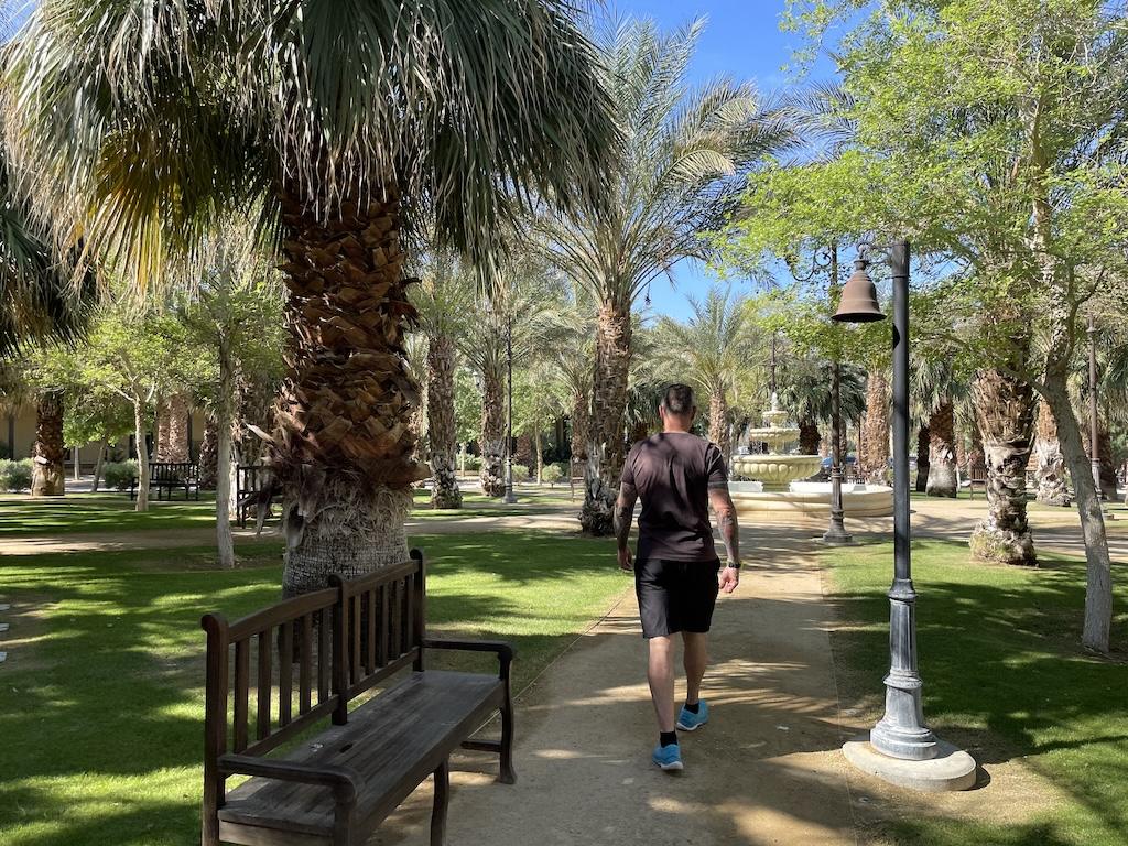 Back view of man walking towards fountain at the Ranch at Death Valley Oasis with palm trees along the path, in Death Valley National Park, California
