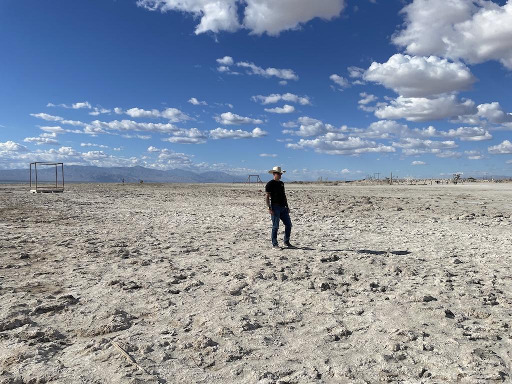 Man standing on the sand with a cowboy hat at Bombay Beach in California