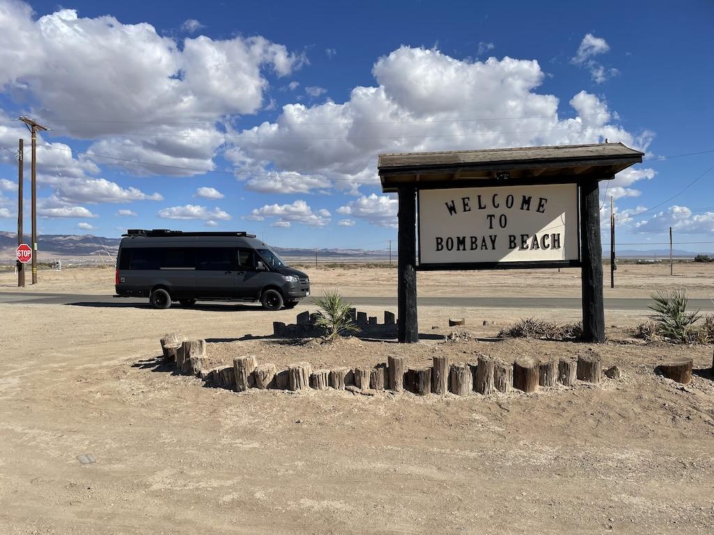 Welcome to Bombay Beach sign and Luna's camper van at the Salton Sea in California
