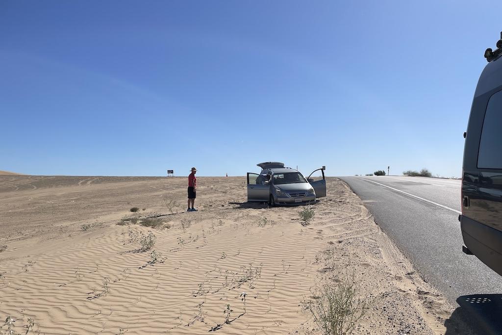 Man walking over to help another man whos car was stuck in the sand at Glamis Sand Dunes, in California