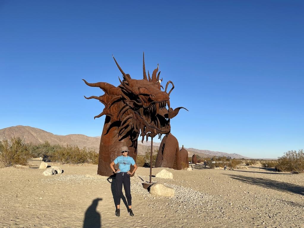 Luna smiling to the camera in front of the serpent metal sculpture at Sky Art desert exhibit in Borrego Springs, California