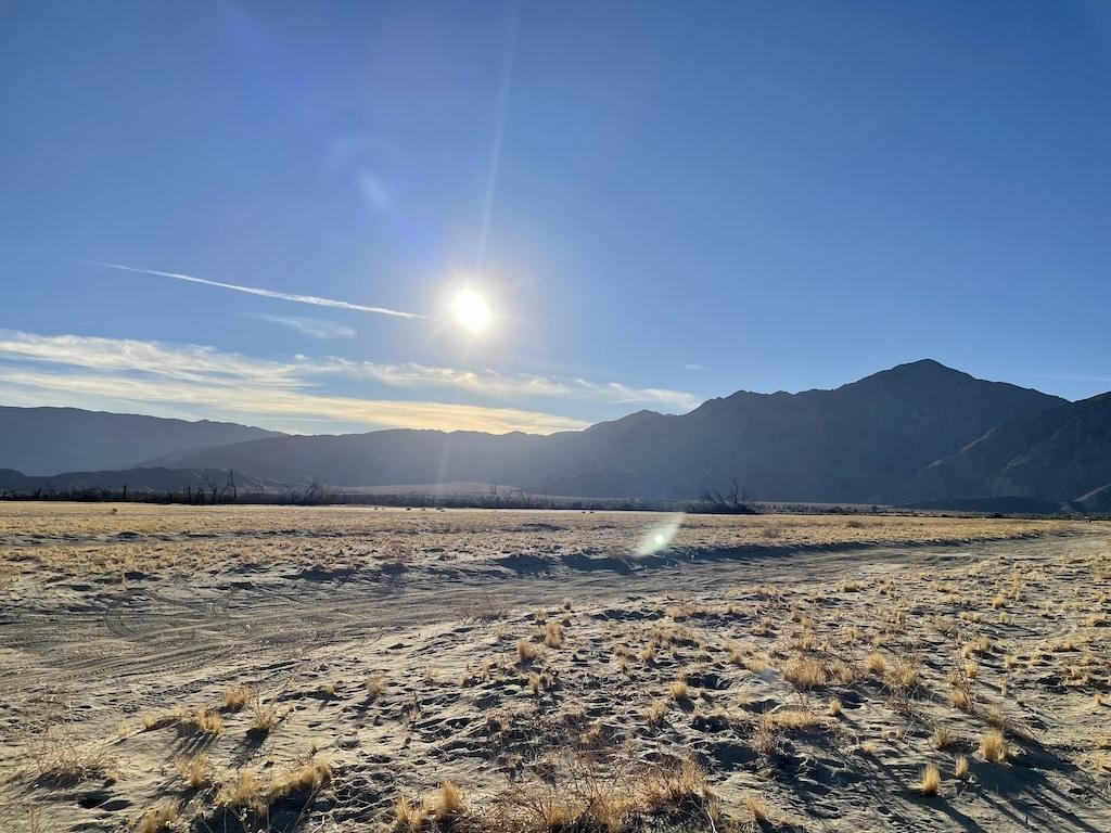 View of dirt road with sun in the sky and mountains in the background at Galleta Meadows, California