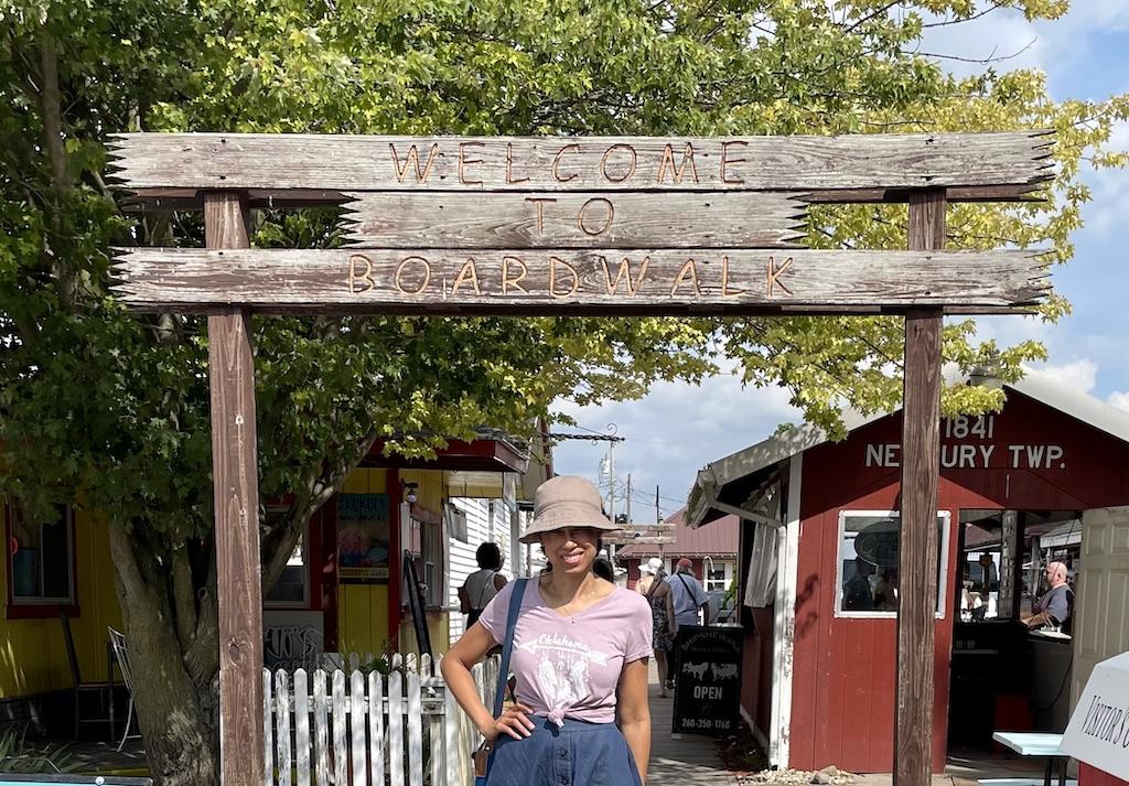 Luna smiling to the camera standing under the Welcome to Boardwalk sign in Shipshewana, Indiana