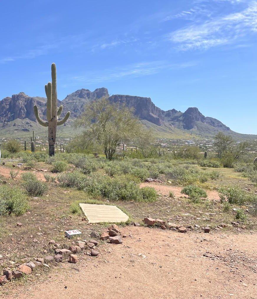 View of Superstition Mountains in background with man on the side taken from the Lost Dutchman museum in Arizona