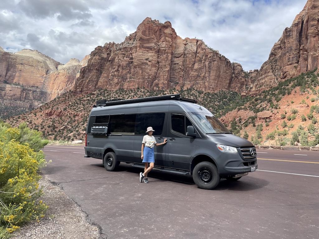 Luna smiling to camera standing in front of Sprinter van at Zion National Park, Utah